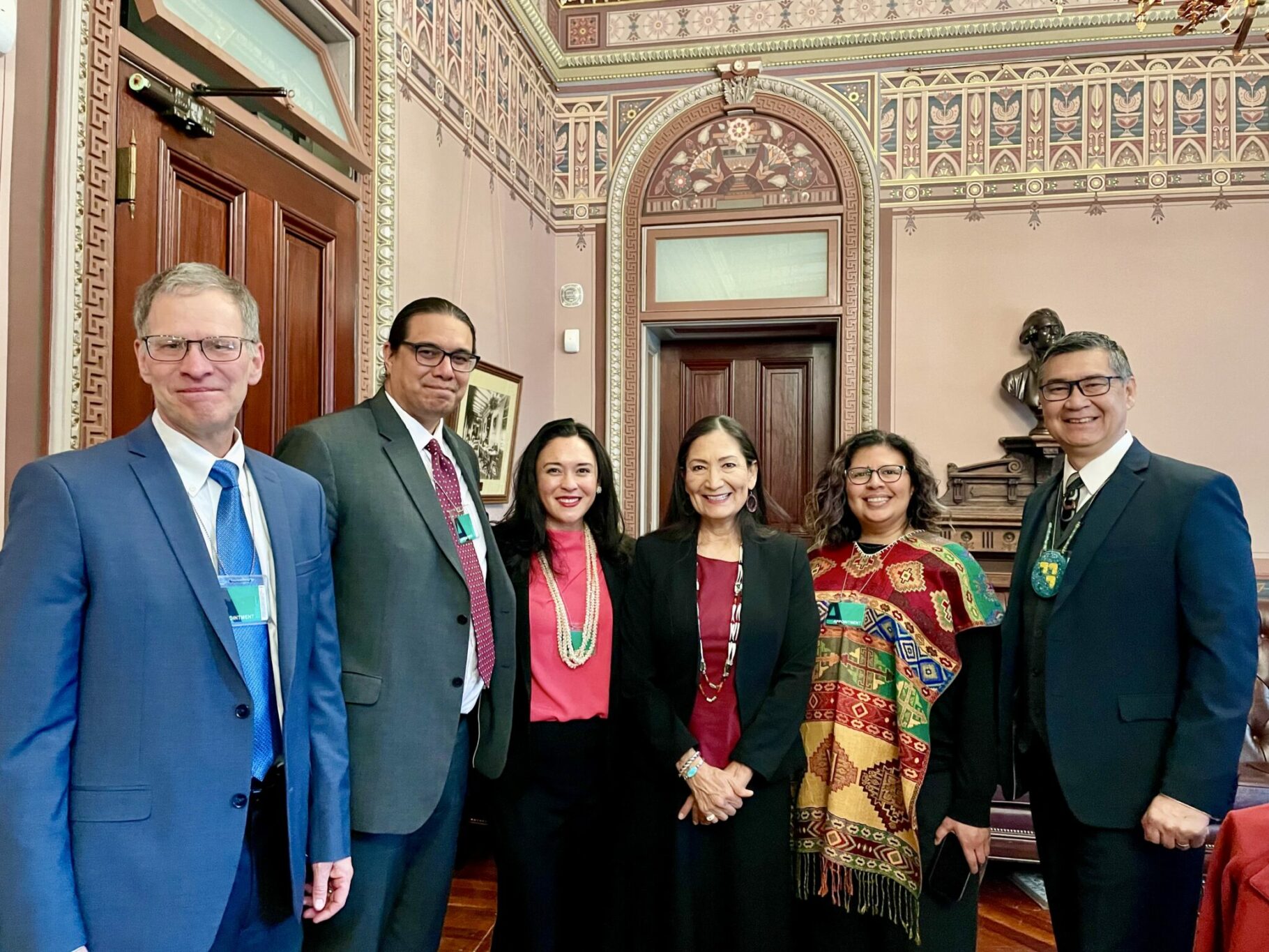 Six people in an ornate room smile into the camera. L–R: Kevin Walker, CEO of Northwest Area Foundation; Wizipan Garriott, Principal Deputy Assistant Secretary for Indian Affairs, U.S. Department of the Interior; Lauren Grattan, Mission Driven Finance; Secretary Deb Haaland, U.S. Department of the Interior; Rosa Cabrera, Chan Zuckerberg Initiative; Ted Piccolo, Mission Driven Finance