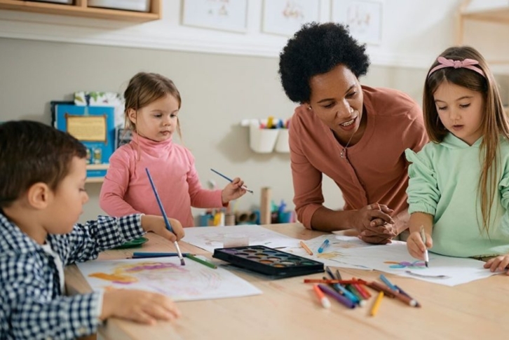 three children with an adult doing art activities at a table