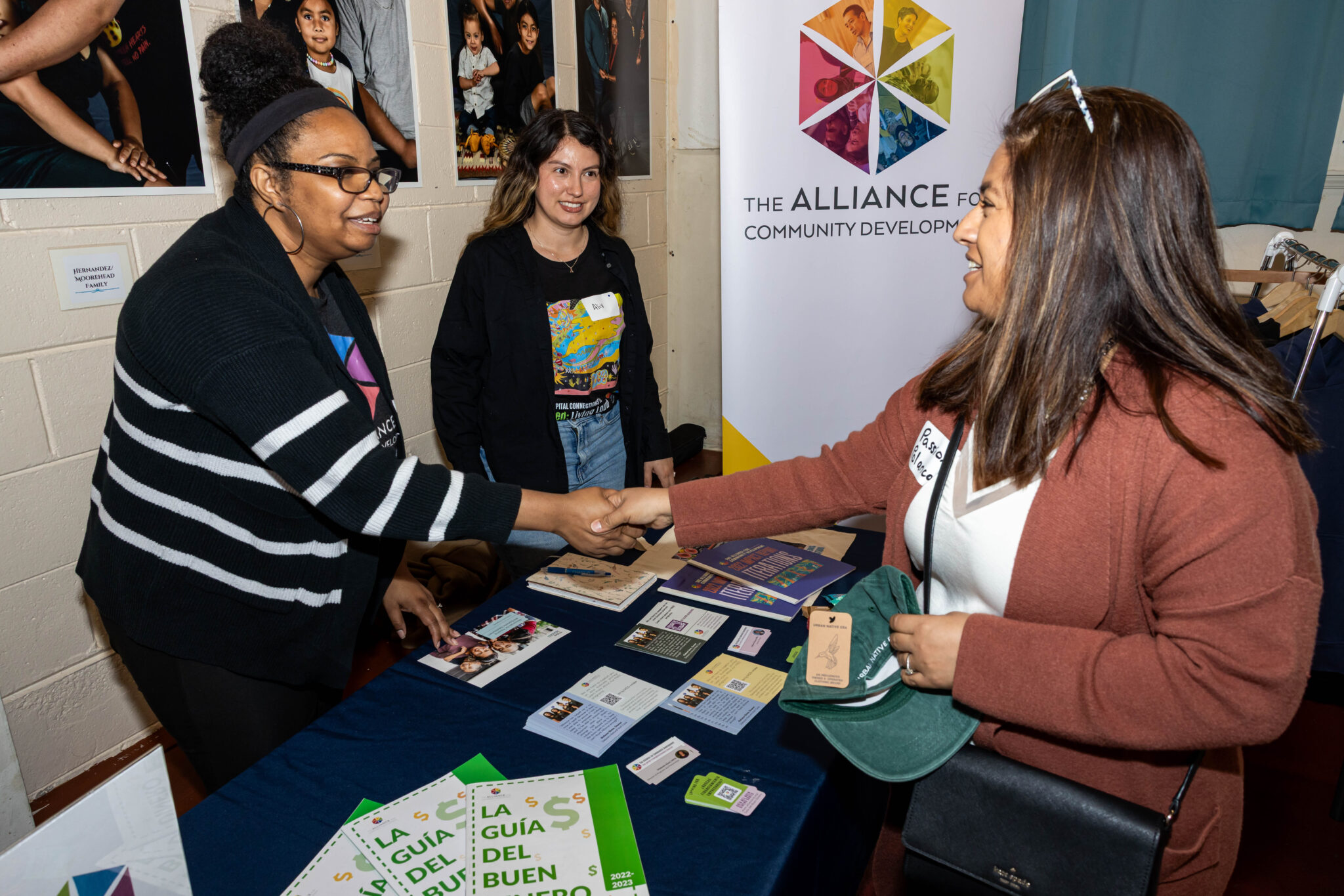 Two women shake hands at a table for The Alliance for Community Development at Trading at the Bay