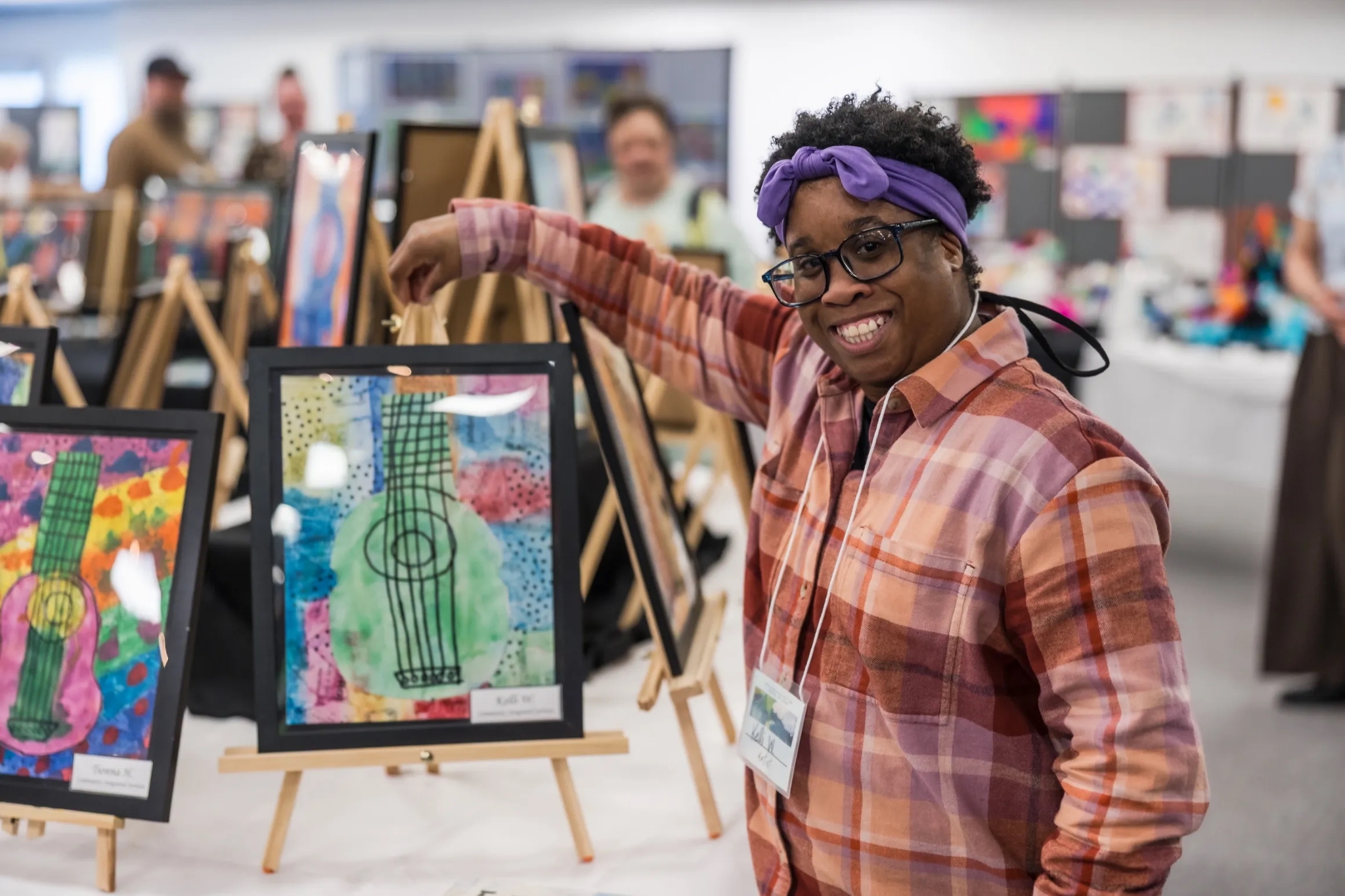 EXCEED-art-show A woman wearing a purple headband stands next to a piece of art